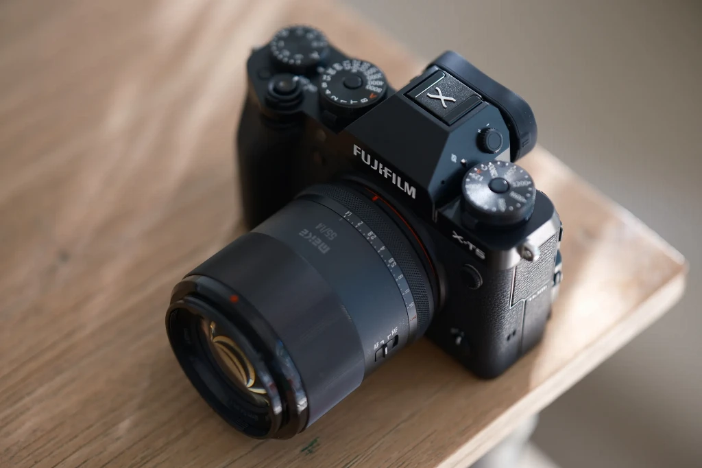 Черный объектив Meike AF 55mm f/1.4 на беззеркальной камере Fujifilm X-T5 с отдельным кольцом диафрагмы и переключателем AF/MF на деревянном столе